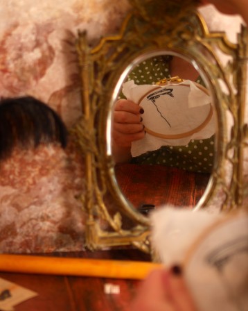 Personne en train de broder qu'on aperçoit dans un miroir dévoilant l'envers de la broderie.